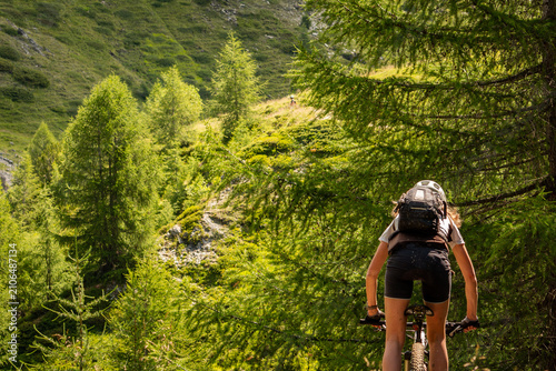Fotografía Outdoor adventure in the Italian Alps, featuring a cyclist on a scenic woodland trail beneath towering alpine trees