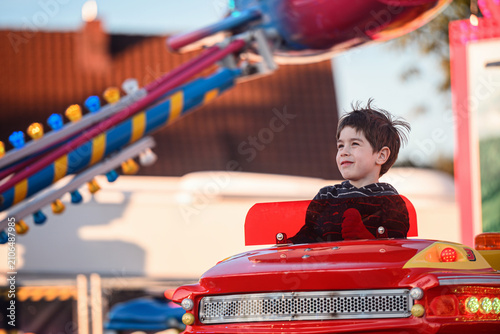 Happy child looking up while riding colorful amusement park carousel at sunset