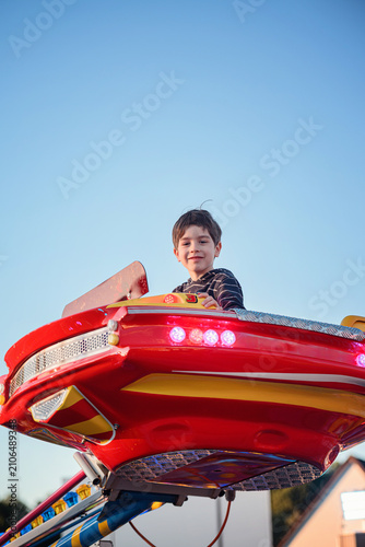 Low angle boy on high flying red amusement park car ride against blue sky