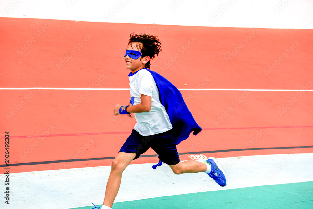 Fototapeta premium Child in superhero costume running on a track, wearing a blue cape.