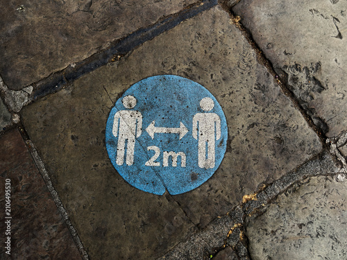 Social distancing 2m floor sticker on stone pavement in Liverpool, UK indicating public health safety for pedestrians and urban street guidance