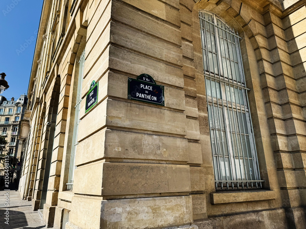 Fototapeta premium Sunlit stone facade at Place du Panthéon corner in Paris, France showing arched windows and neoclassical architecture on a clear blue day