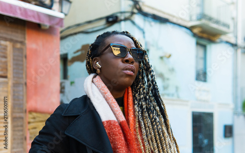 Black woman wearing earbuds and sunglasses in city street
