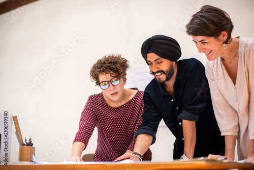 Photography Three colleagues collaborating on a project at a desk, smiling.