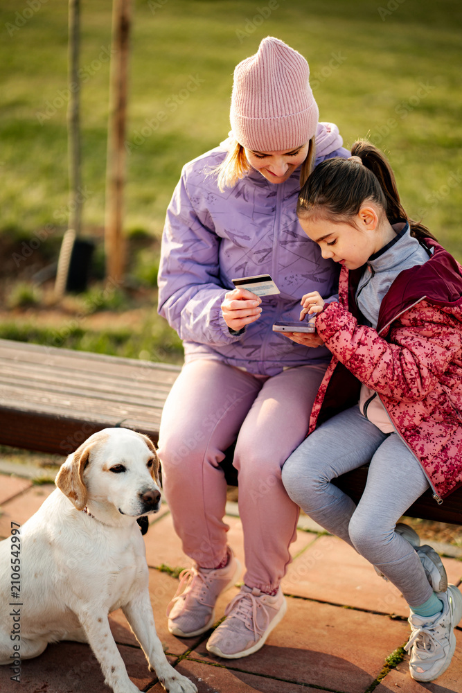 Fototapeta premium Mother and daughter using credit card for online shopping in park