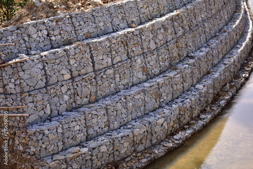 Retaining wall constructed from gabion baskets filled with stones viewed from the side outdoors, Gabion retaining wall