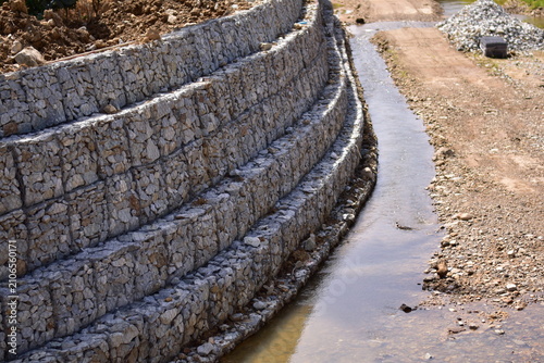 Retaining wall constructed from gabion baskets filled with stones viewed from the side outdoors, Gabion retaining wall
