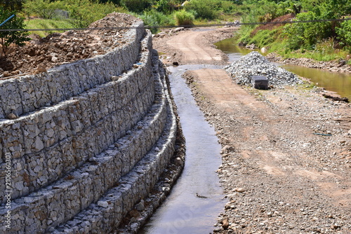 Retaining wall constructed from gabion baskets filled with stones viewed from the side outdoors, Gabion retaining wall