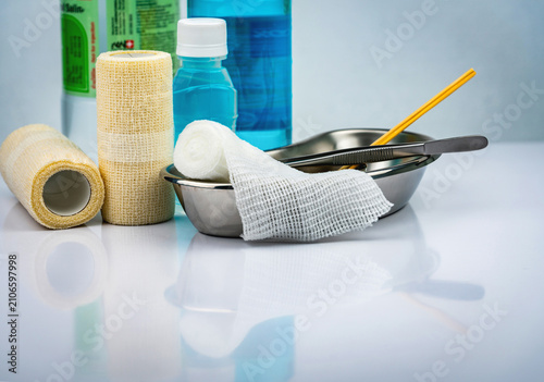 Billede på lærred Sterile wound dressing supplies with gauze bandages, stainless steel basin, forceps and antiseptic solution arranged on a clean white surface for hospital, clinic and first aid healthcare concepts