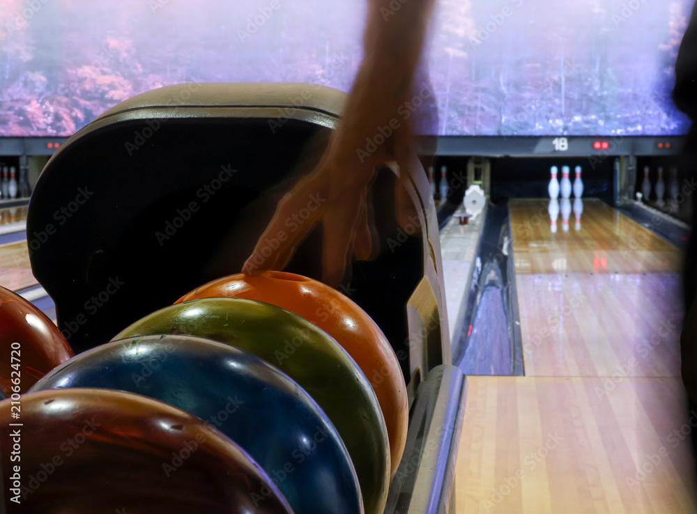 Fototapeta premium Person picking up a bowling ball from the ball return in an indoor bowling center. Horizontal format