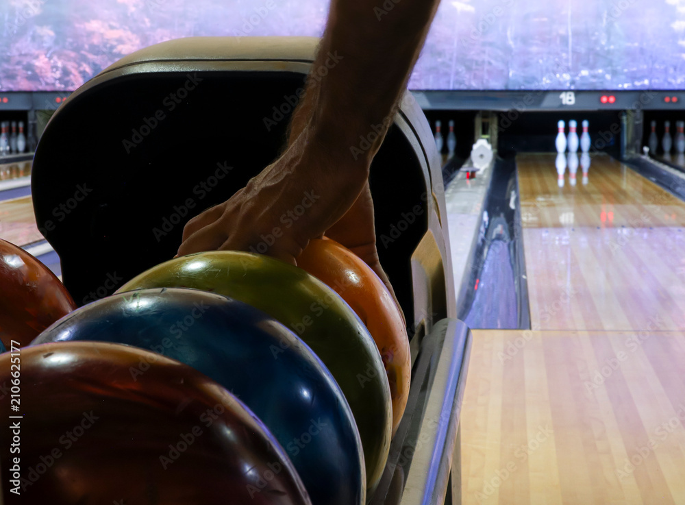 Fototapeta premium Person picking up a bowling ball from the ball return in an indoor bowling center. Horizontal format