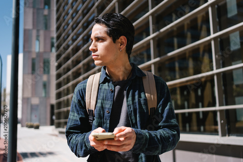 Young hispanic man using mobile phone in modern urban city. Happy university student smiling at campus