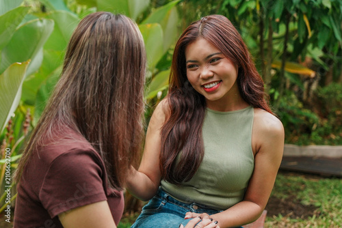 Two smiling young Asian girls are sitting together in the garden and telling stories.
