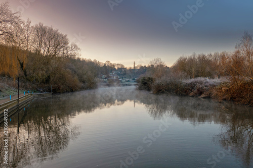 Peaceful River with Morning Mist and Reflections of Bare Trees in Winter