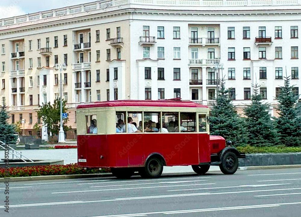 Obraz premium Vintage red and cream retro bus with tourists driving on Independence avenue in Minsk Belarus for historical city excursion banner post-soviet travel guide and transport heritage poster design