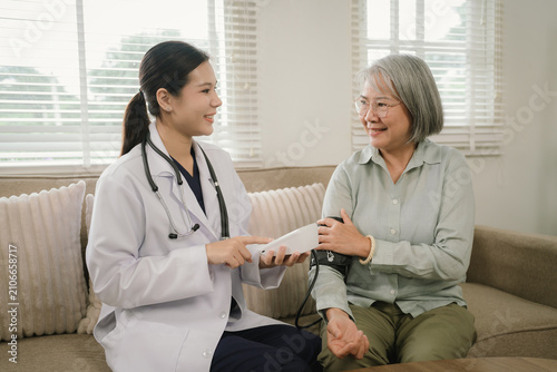 Young female doctor measures an elderly woman's blood pressure during a friendly home healthcare visit, promoting healthy aging and wellness.