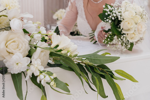 Quadro su tela A close-up shot of a bride signing the wedding contract or certificate during the marriage ceremony, accompanied by a beautiful white rose bouquet and floral decorations on a white table