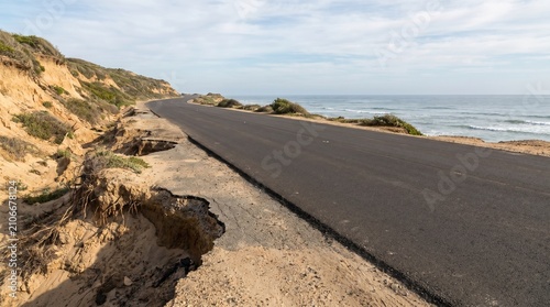 Coastal road erosion, Washed out sandy shoulder, Super El Niño infrastructure risk, Shoreline retreat scene, Clean transport landscape