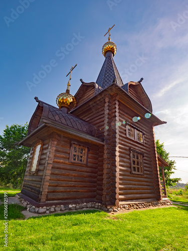 Schilderij op canvas Traditional Russian wooden Orthodox church with golden onion domes and log walls under a clear blue sky