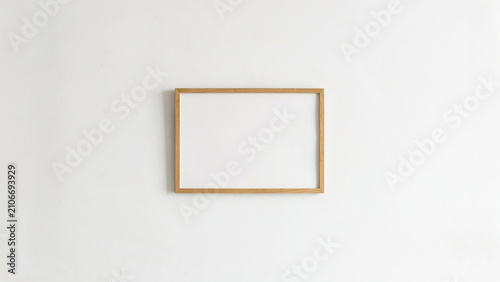 Horizontal wooden picture frame mockup centered on a plain white wall with horizontal landscape interior minimalist template