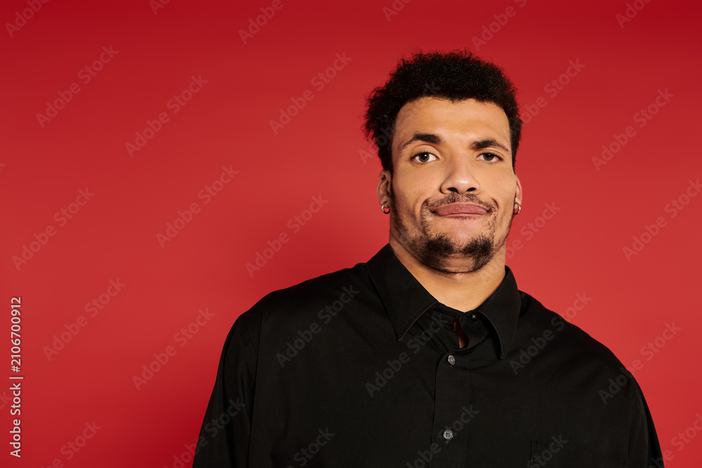 Fototapeta premium Young handsome man stands with a relaxed expression in front of a bold red backdrop.