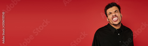 Obraz na płótnie Handsome young man makes a playful gesture while posing in a studio with red backdrop