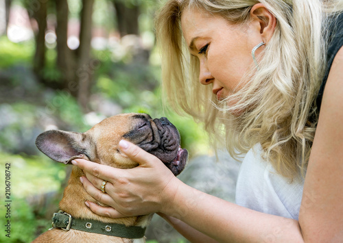 Affectionate woman holding adorable French bulldog in peaceful nature