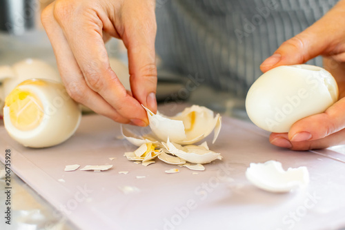 Bild auf Leinwand Hands peeling hard boiled egg on cutting board