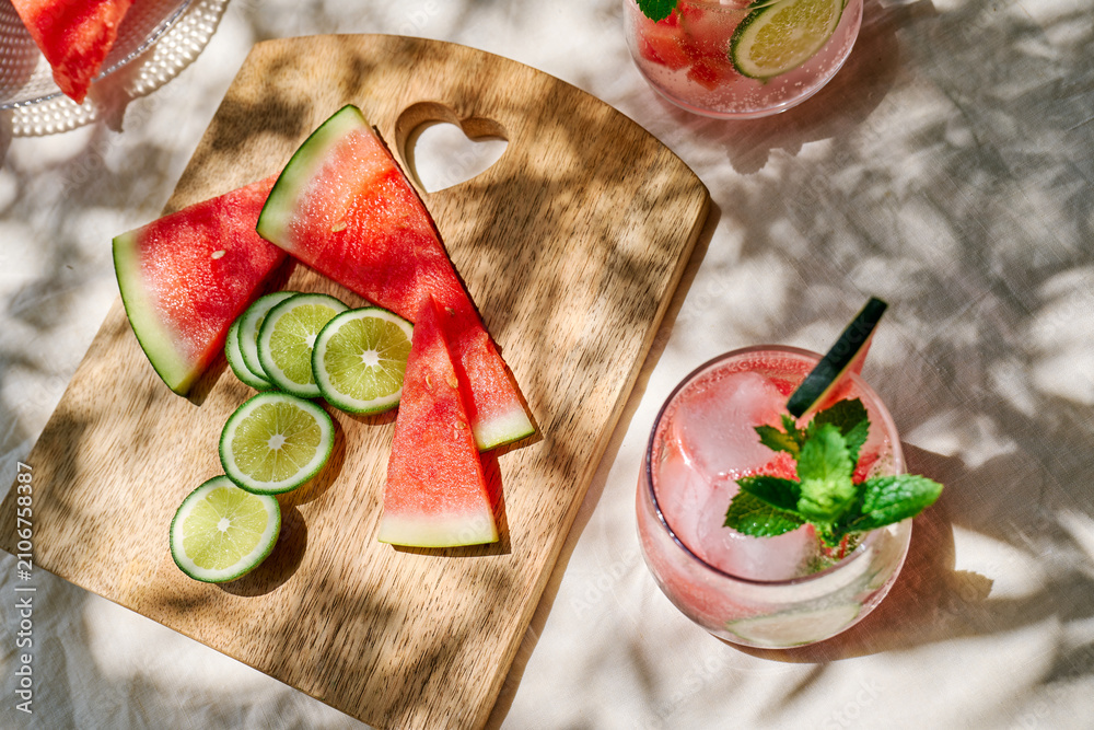 Obraz premium Summer refreshing watermelon drink with ice, mint and slices of lime on the table in the garden. Fresh healthy cold melon beverage. Fruit infused water, herbs and lemon.