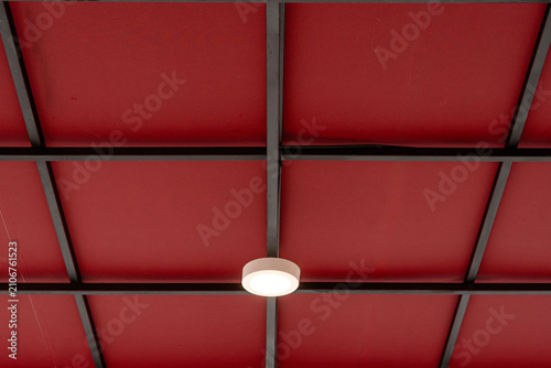 Red ceiling with black metal grid framing and round white light fixture.