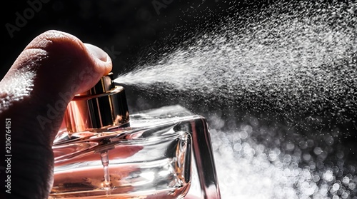 Close-up of a hand spraying fragrance from a luxury perfume bottle, creating a fine mist against a dark background