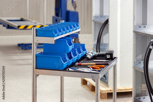 Foto Rolling workbench tool storage system with two shelves adorned with blue plastic bins and tools like cordless drill, wrenches, a hammer, screwdrivers and pliers