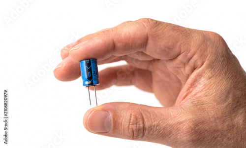 Person Holding Blue Electrolytic Capacitor on White Background