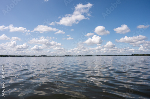 Wide view over a calm lake under a clear sky with scattered white clouds, the view of the Zwischenahner Meer, 26160 Bad Zwischenahn, Germany