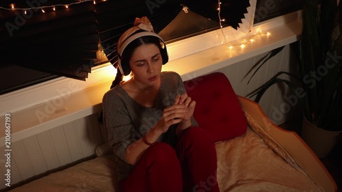 Top view mid shot of a young Caucasian woman wearing headphones, listening to music and staring blankly into the distance while scratching her hand with her fingers. Anxiety, nervous habits
