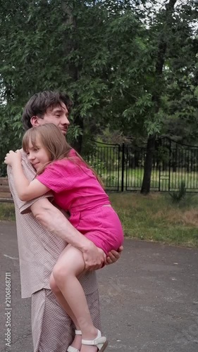 Happy father holding and spinning with his little daughter while walking together in a green park