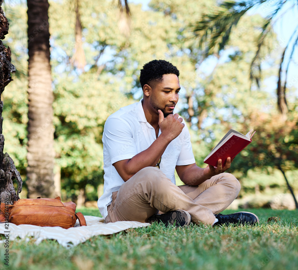 Fototapeta premium Young man student businessman enjoys sunny day while reading a book in park, highlighting his joy and connection to the world around him