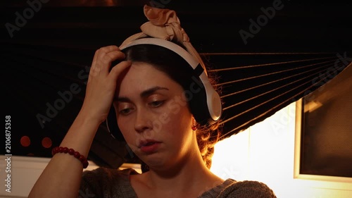 Portrait of a young Caucasian woman wearing headphones, listening to music and staring blankly into the distance while nervously touching her face. Anxiety, neurotic behavior, psychological distress