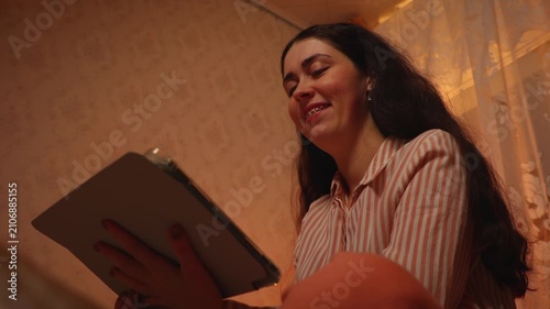 Young Caucasian woman with braces relaxing and smiling while watching an online video on a tablet in the evening. Digital entertainment, home leisure, dental care journey
