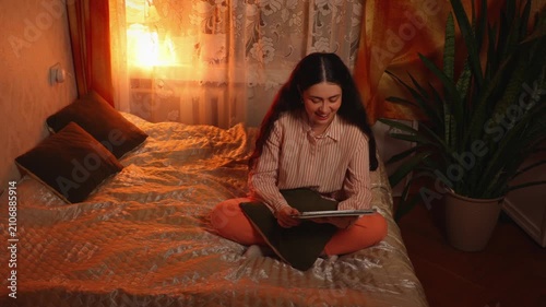 Top view of a young Caucasian woman with braces relaxing and smiling while watching an online video on a tablet in the evening. Digital entertainment, home leisure