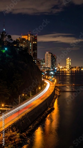 A nighttime cityscape with a road winding along a body of water