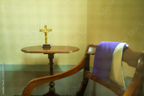 Golden Crucifix on Wooden Table Next to Confessional Chair with Priest Stole