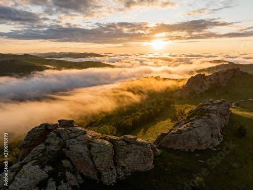 Sunrise over mountain peaks with sea of clouds and rocky outcrops