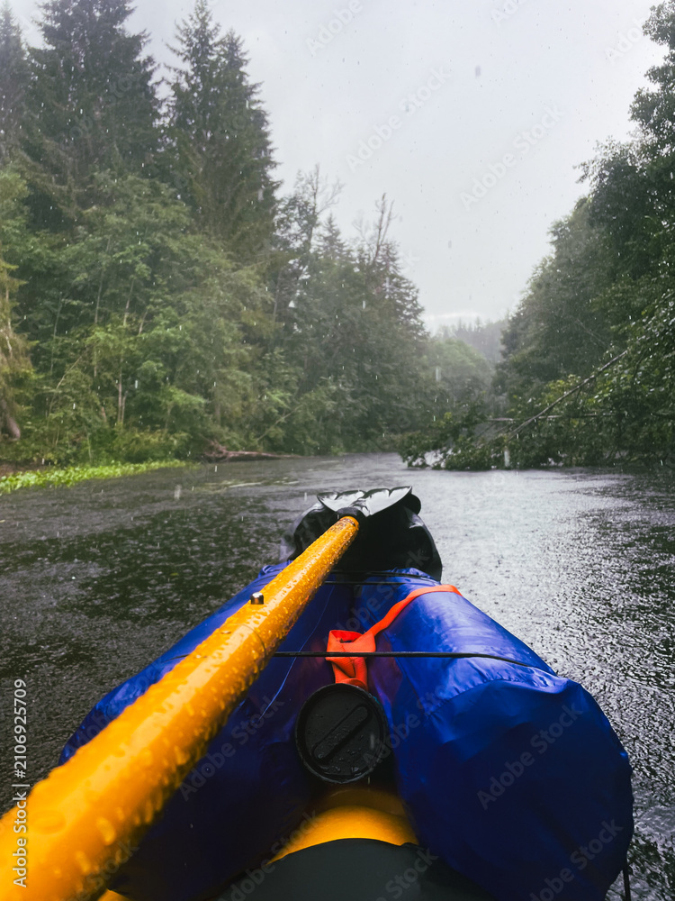 Fototapeta premium POV kayaking through rainy forest river during wilderness adventure