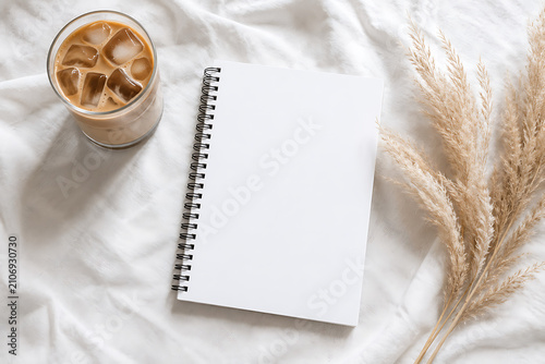 Minimalist blank notebook mockup on white bed sheets, iced coffee latte in glass, dried pampas grass decor, aesthetic morning journaling concept isolated on White Background ai