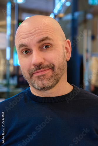 Skeptical mature bald man raising eyebrow with doubtful amused expression indoors