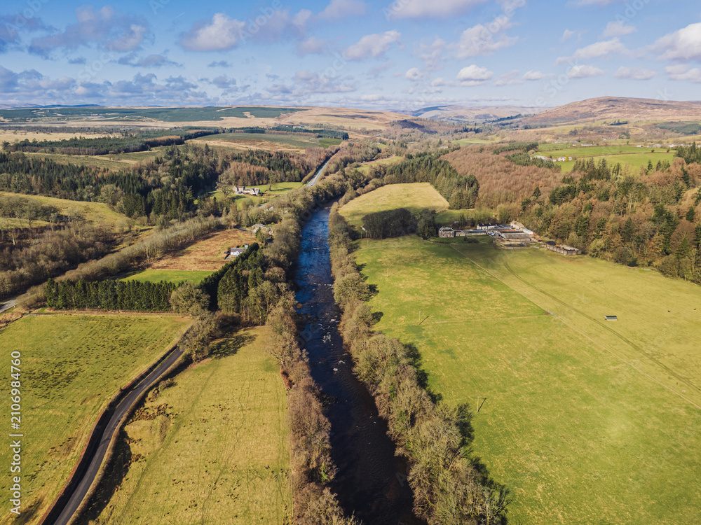 Obraz premium The River Esk winds through green fields and dense trees near Langholm in the Scottish Borders. This scene shows a clear view of the landscape near Langholm on the A7