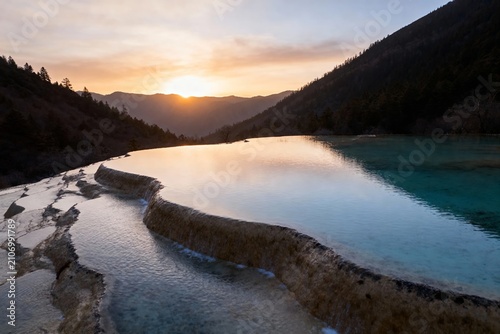 Sunset over a serene mountain lake with terraced mineral formations reflecting golden light