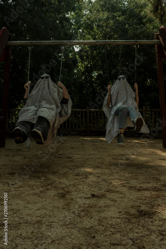 Two People in Ghost Costumes on Swings in Playground