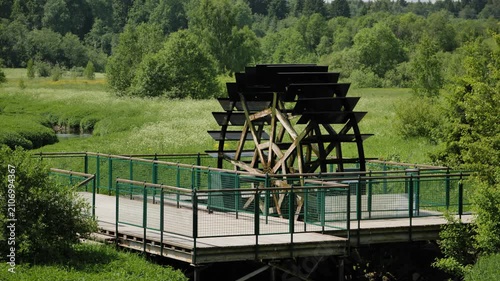 Water wheel turning over river within a lush green forest landscape